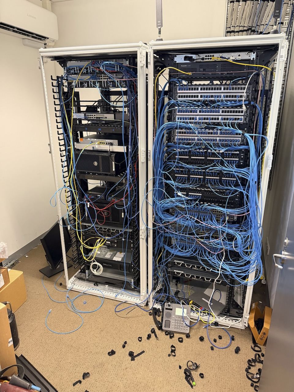 Comms rack before remediation - cabling untied, unlabelled and running across the floor